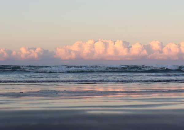 Fluffy pink clouds at sunset, over waves with reflection of pink on the sand