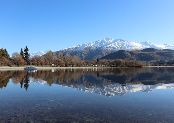 snowy mountains reflected in a lake with trees and a boat