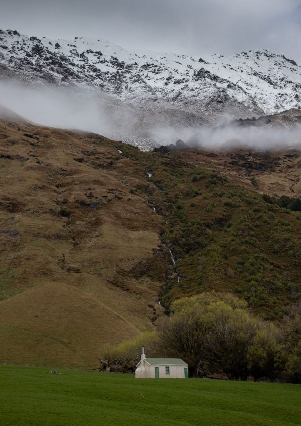 lonely house surrounded by tall mountains, snow and misty clouds. green everywhere